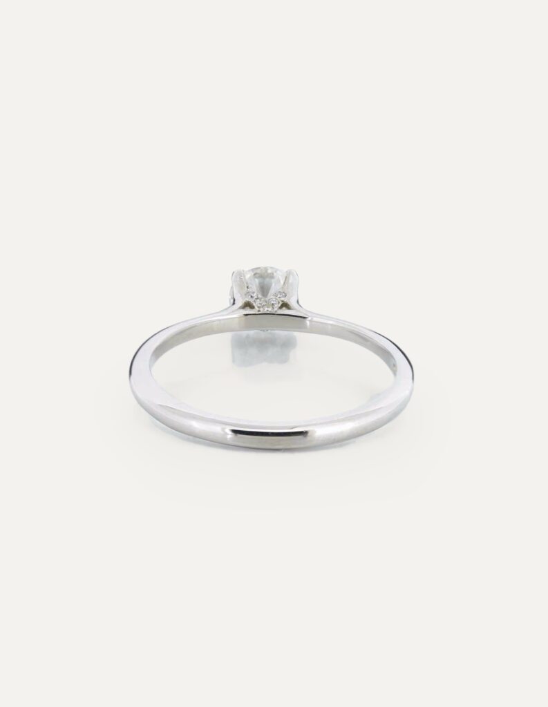 Side view of a platinum solitaire ring with a 4-claw set round diamond and diamond-set collet