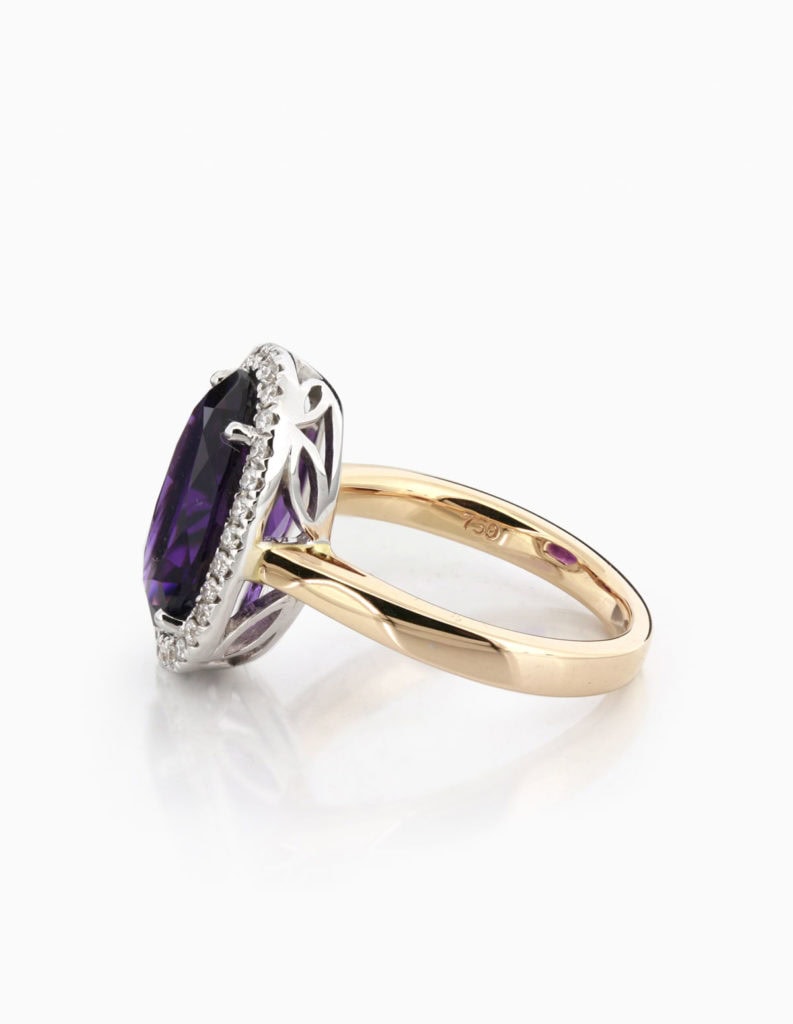 Angled view of an 18ct yellow gold amethyst halo ring showing the diamond-set gallery