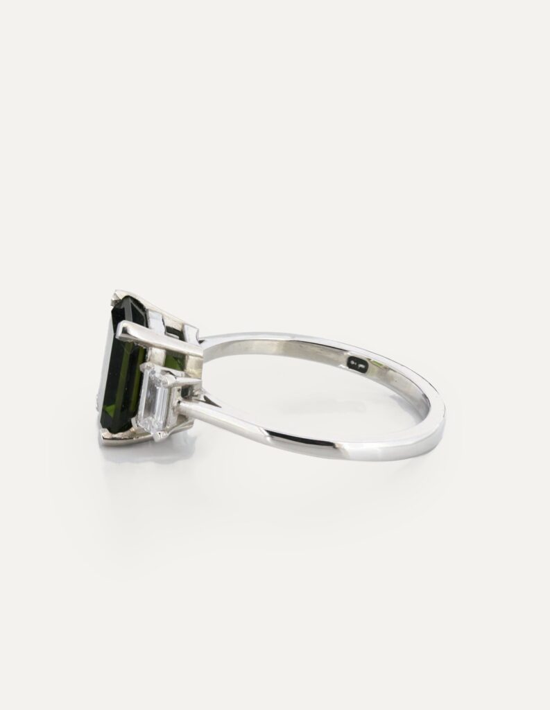 Side view of an 18ct white gold three-stone ring with an emerald-cut green tourmaline and diamonds