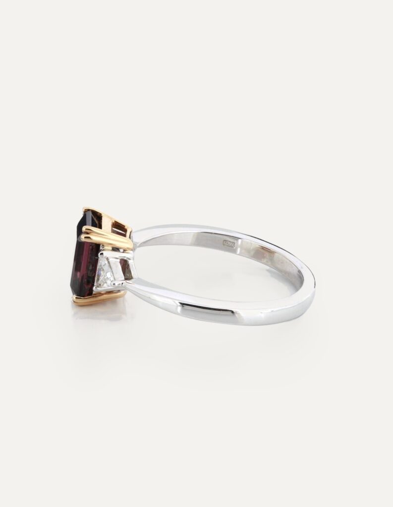 Side view of an 18ct white gold three-stone ring with an emerald-cut garnet and trillion diamonds, showing a rose gold gallery