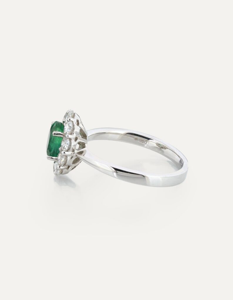 Side view of an 18ct white gold cluster ring with an oval emerald and diamond halo