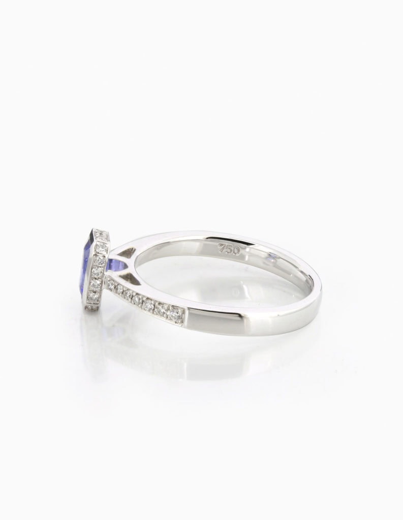 Side view of an 18ct white gold dress ring with a bezel-set emerald-cut tanzanite and pave diamond shoulders