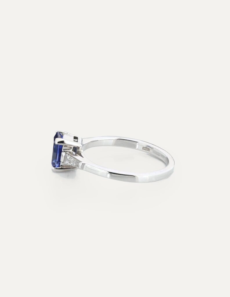 Side view of an 18ct white gold dress ring with an emerald-cut tanzanite and tapered baguette diamond shoulders
