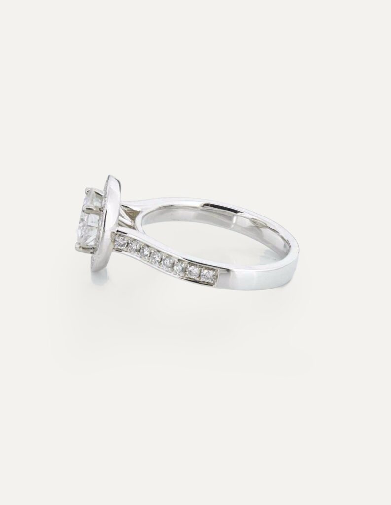 Side view of a platinum halo ring with a round brilliant diamond and pave diamond shoulders