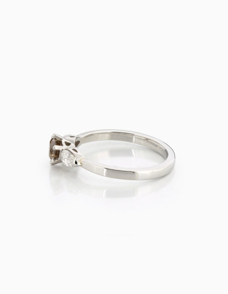 Side view of a platinum three-stone ring with a round brilliant diamond and pear-shaped diamond shoulder