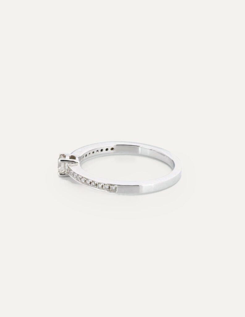 Side view of an 18ct white gold ring with a claw-set round diamond and pave diamond shoulders