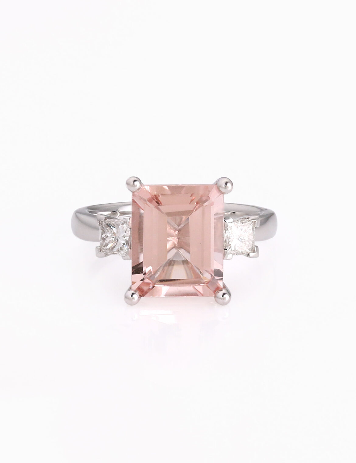 A large emerald cut pink stone ring with princess cut diamonds either side of the central morganite stone all set on a white band