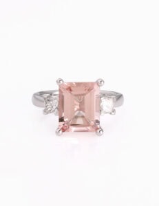 A large emerald cut pink stone ring with princess cut diamonds either side of the central morganite stone all set on a white band