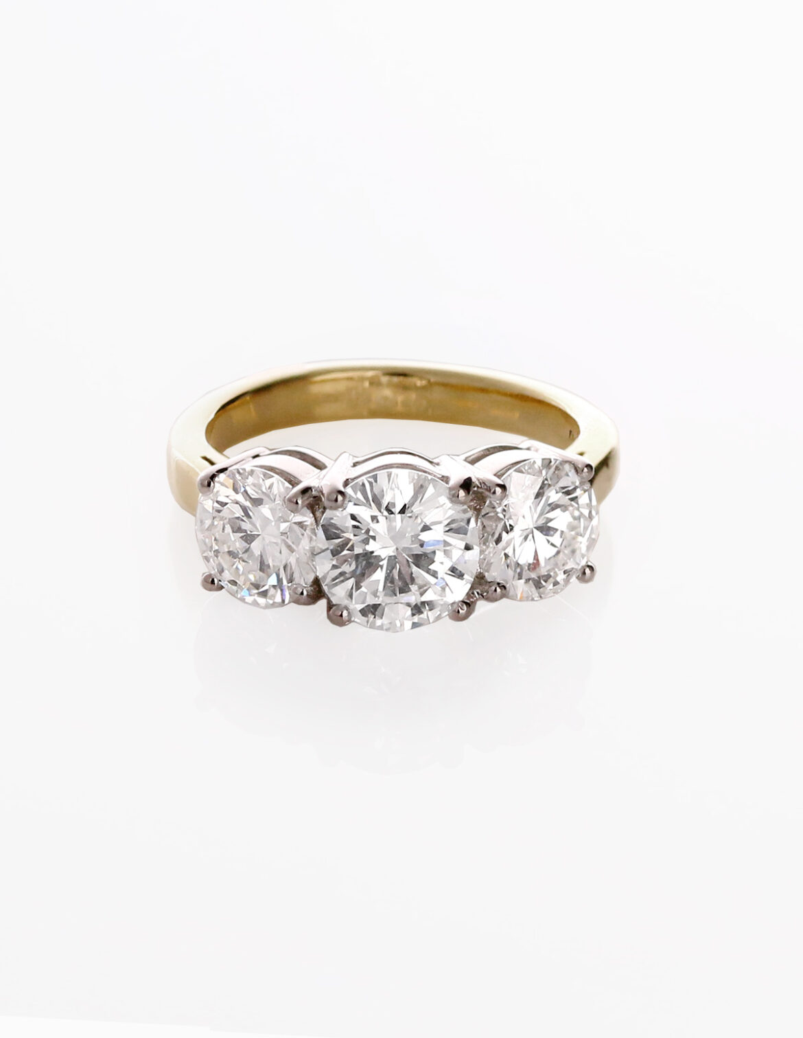 A large 3 stone diamond ring with yellow gold band is in the centre of a white background