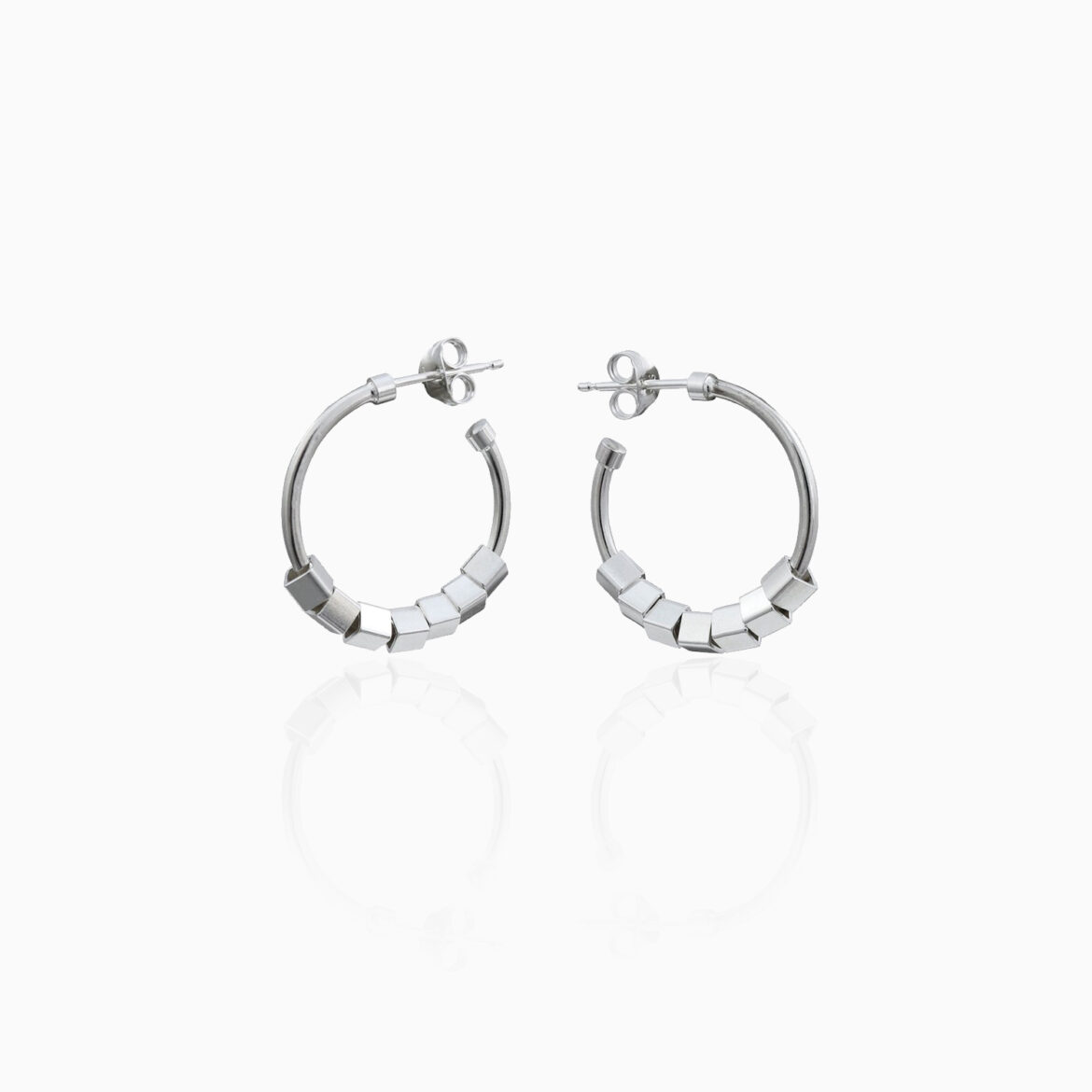 A pair of silver hoop earrings with a cube design are centred on an off white background.