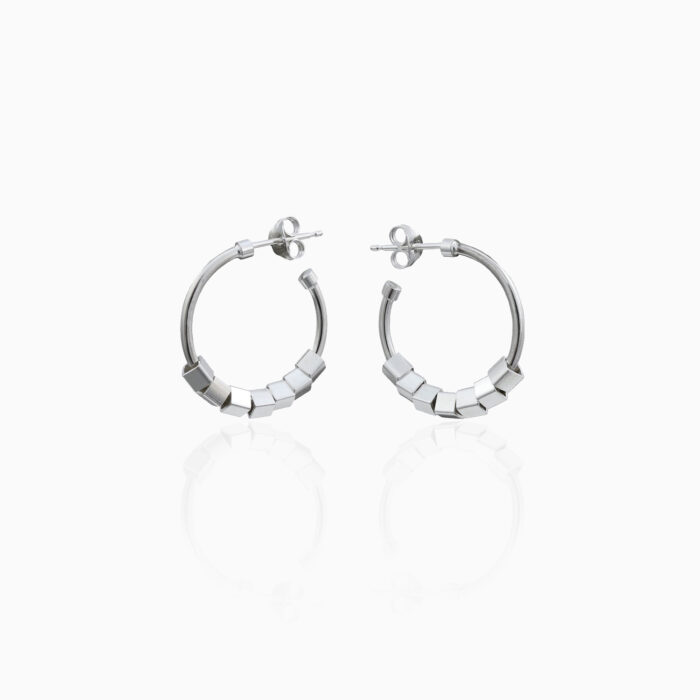 A pair of silver hoop earrings with a cube design are centred on an off white background.