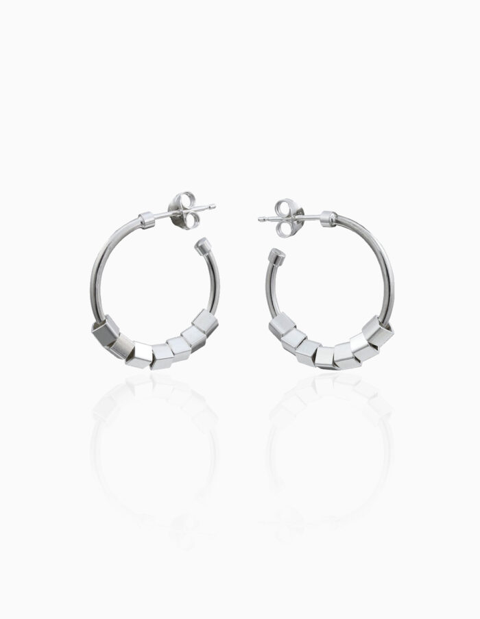 A pair of silver hoop earrings with a cube design are centred on an off white background.