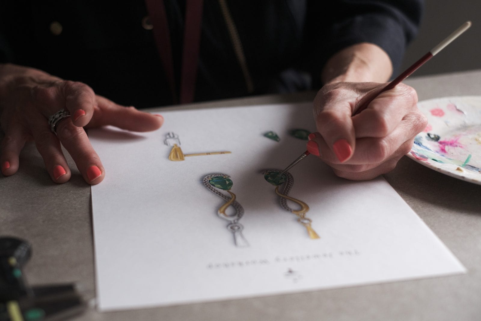 Yvonne hand-painting a watercolour illustration of a bespoke emerald pendant and earrings design