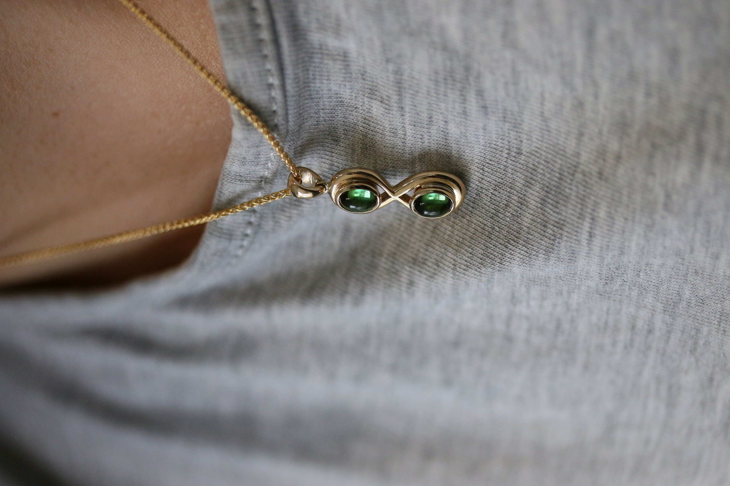 One-off 9ct gold infinity pendant set with two green tourmaline cabochons on a spiga chain